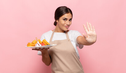 young hispanic woman smiling happily and cheerfully, waving hand, welcoming and greeting you, or saying goodbye