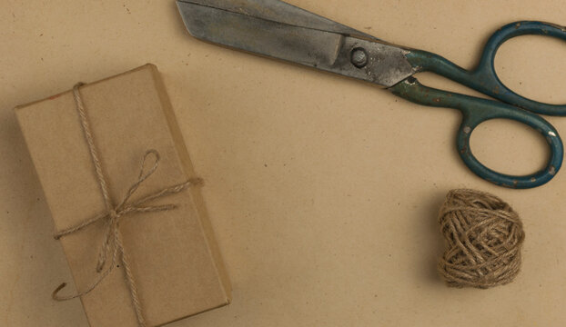 Twine, scissors and gift box on a craft paper background. View from above. Eco-friendly packaging made from natural materials.