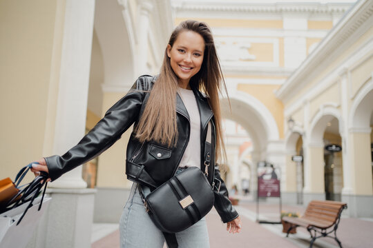 Holds Several Different Sizes Of Bags With Clothes In His Hands. Black Leather Jacket, Milennial, Brunette. Shopping Online Store, A Young Woman Is Shopping At Her Favorite Clothing Stores