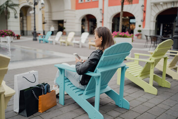 shopping at an outlet, a woman has made several purchases of clothing items, is sitting in the phone app selects more brands for purchases. Colored chairs comfortable waiting time