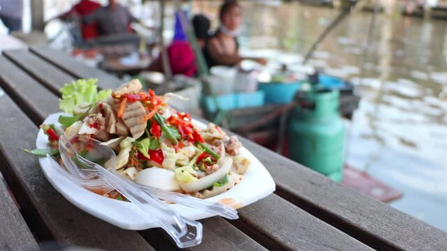 The spicy vietnamese sausage salad on dish with blurred kitchen on boat at background, Khlong Lat Mayom Floating Market, Thailand.