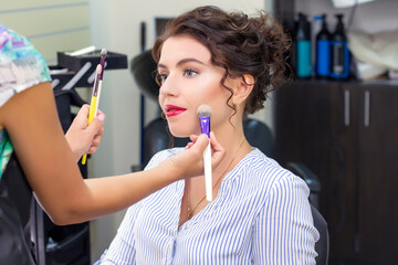 Make up artist applies a light layer of matte powder using a professional makeup brush. girl at makeup artist