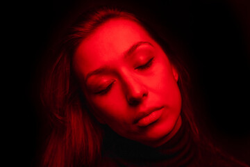 Low key full-face close up portrait of tired sleepy girl closed eyes in creepy red light. sleeplessness, Insomnia, nightmares, stress-induced mental disorders concept. Lack of sleep can cause fatigue