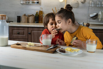 Children spread chocolate paste on toast bread in the kitchen background. Breakfast happy family having fun with food