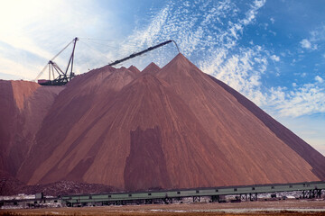 Extracting and mining potassium salts. Large excavator machine and Huge mountains of waste ore in the extraction of potassium against the backdrop of sky. Belarus, Soligorsk.
