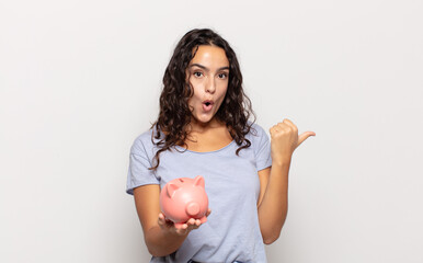 young hispanic woman looking astonished in disbelief, pointing at object on the side and saying...