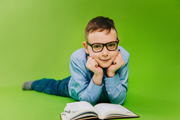 A boy in a blue striped shirt wears black glasses and reads a book. Child with poor eyesight...