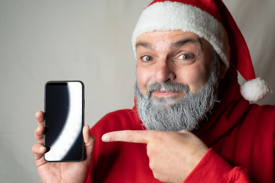 Santa Claus points his finger at a cell phone and is delighted.