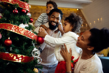 Happy black family having fun while decorating Christmas tree at home.