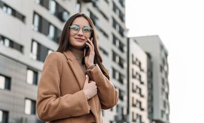 Happy pretty brunette girl using mobile phone near office, beautiful woman browsing phone and doing online shopping in a mobile app while smiling walking near shopping mall.