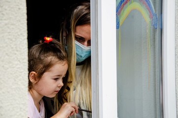 Mom and daughter are in quarantine during the new wave of coronavirus. A child and mother look out...
