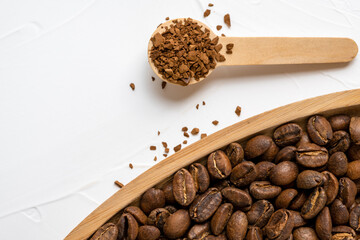Instant coffee granules in a wooden spoon and roasted coffee beans in a plate on white background....