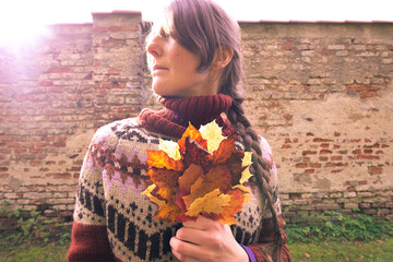 Frau in einem gemusterten Wollpullover und einem geflochtenen Zopf einen bunten Herbststrauch...