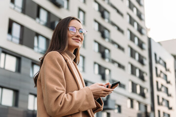 Business Woman walking down the city street and talking on mobile phone. Female business professional walking outside with an office building in background.