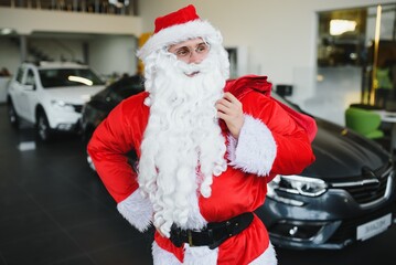 New car as a Christmas present. Santa Claus in the car showroom near a new car.
