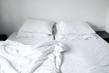Fototapeta na wymiar Messy and unmade double beds white pillow and blanket on bedroom hotel, Interior white room in cloudy day 