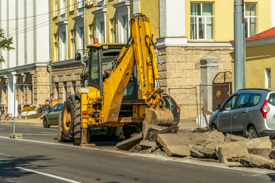 Yellow excavator with bucket lifts the asphalt to repair the roadway on a Sunny day