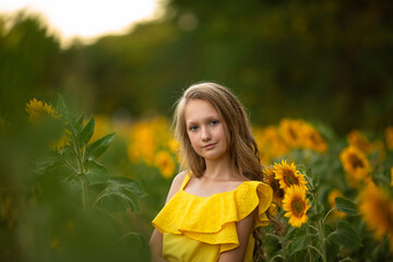 Cute teenage girl in yellow dress on the field with sunflowers