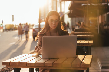 Close-up of young professional business woman using her laptop outside while working at modern business center, modern buildings in the background.