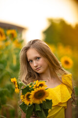 Naklejka premium Cute teenage girl in yellow dress on the field with sunflowers
