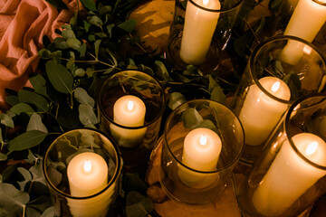 Romantic wedding display of wax candles glowing with small flames in glass vases centrepieces
