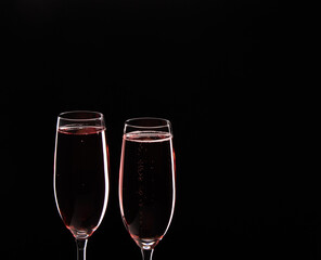 Two glasses of rose champagne with rim lights on black background.