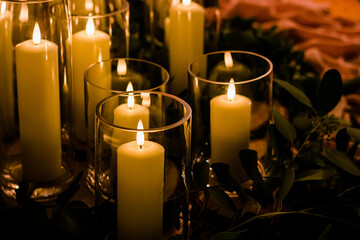 Romantic wedding display of wax candles glowing with small flames in glass vases centrepieces