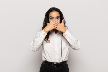 young hispanic woman covering mouth with hands with a shocked, surprised expression, keeping a...