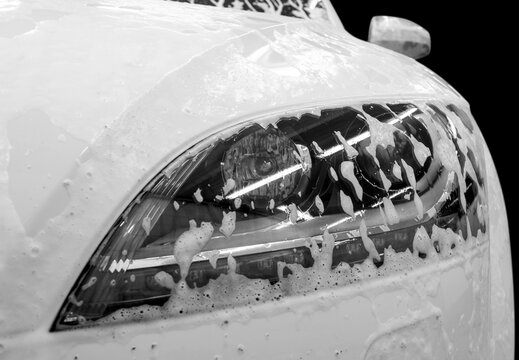 Auto headlamp covered by foam. Modern car wash with soap.