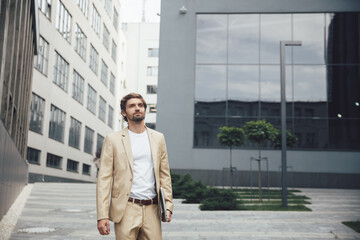 Successful businessman carrying laptop near modern building