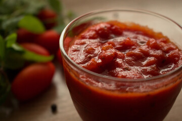 Close up of Neapolitan tradition tomato sauce for pasta or pizza in a glass bowl on a wooden background. Cooked with tomatoes, peppers, oil, garlic, tomato paste, oregano, onions and basil.