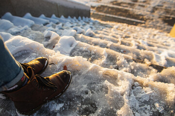 Danger of slipping. Female boots on rough slipper ice surface. A woman in brown leather shoes...