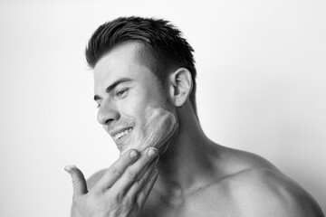 Fototapeta na wymiar Muscular sexy model sports young man. Black and white portrait of beautiful smiling healthy guy applying foam for washing on his face. Facial skincare routine.