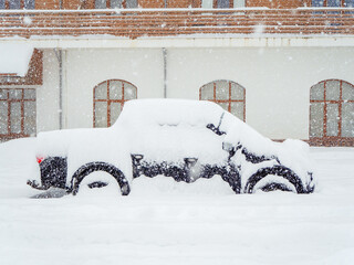 Retro car stands covered with snow in front of the building during heavy snowfall