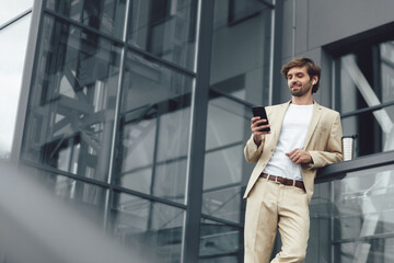 Man in suit posing near office center with smartphone