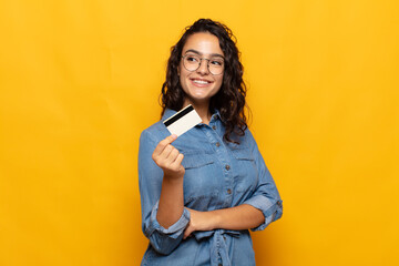young hispanic woman smiling happily and daydreaming or doubting, looking to the side