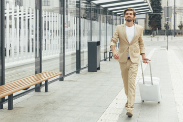 Handsome man in suit standing on bus stop with suitcase