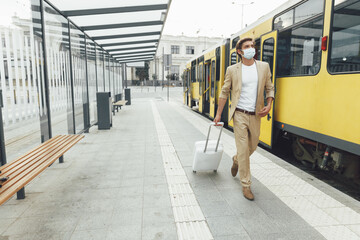 Handsome man in medical mask walking with suitcase outdoors