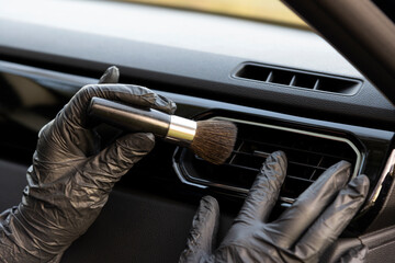 Obraz premium Worker cleaning automobile air conditioner vent grill with brush, closeup. Car wash service