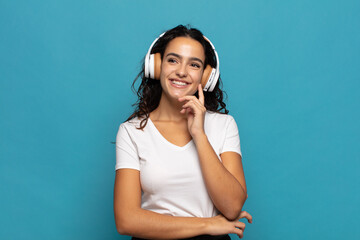 young hispanic woman smiling happily and daydreaming or doubting, looking to the side