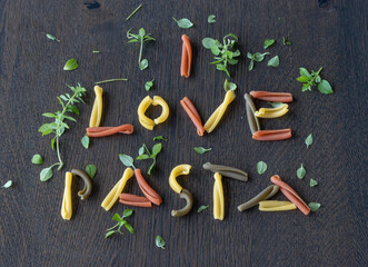 I love pasta written with tricolor caserecce Italian pasta, dressed with basil on a wooden table, top view