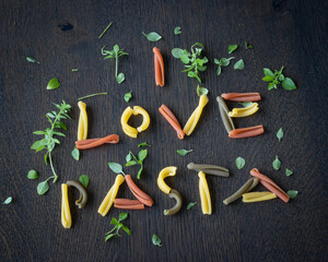 I love pasta written with tricolor caserecce Italian pasta, dressed with basil on a wooden table, top view
