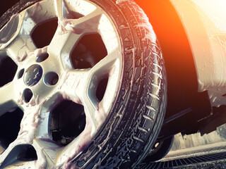 Close up of a car wheel during washing. Cleaning a car tire with  foamy cleanser. Profile view of a...