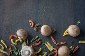 cave mushrooms or chestnut mushrooms with Tricolore Caserecce Italian pasta with 3 colors and dwarf basil leaves as a frame composition on wooden table with space left for text
