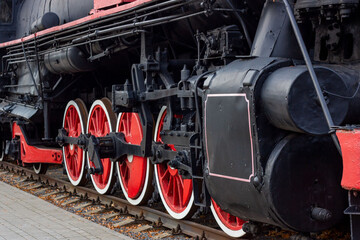 Old black and red retro steam locomotive wheels at the railway station. Vintage train staying on the railroad.