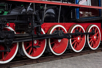 Old black and red retro steam locomotive wheels at the railway station. Vintage train staying on...