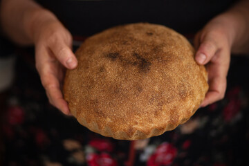 Close-up of fresh homemade bread in mom's hands. A woman holds a loaf of aromatic bread. A loaf of freshly baked bread in the hands of a baker.