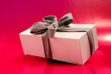 White gift box with gray ribbon and bow on a pink background close-up. Concept of holiday gift for christmas, new year, birthday.