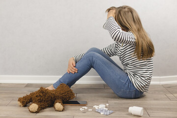 Psychological health of children and adolescents. A depressed girl sits on the floor, pills lie...