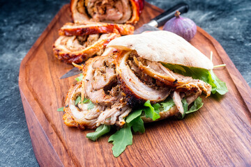 Traditional Italian Porchetta arrotolata pork meat sandwich with pita bread and rocket salad offered as close-up on a modern design wooden board